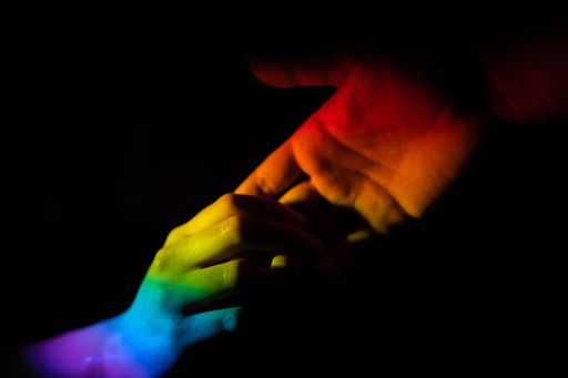 A closeup of a hand helping another illuminated with the LGBT pride flag on black background - love and peace concept