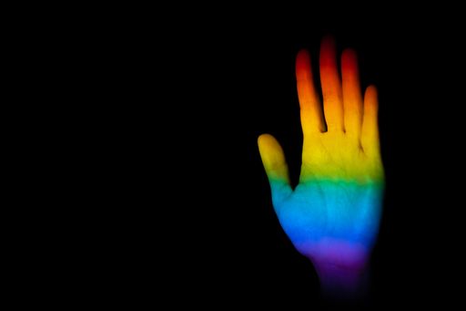 A closeup of a hand making a stop gesture illuminated with the LGBT pride flag on a black background with space for text- equality concept
