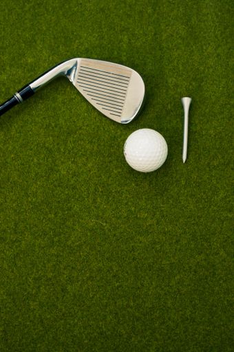 A vertical shot of a golf club, ball, and a tee on the grass with a copy space