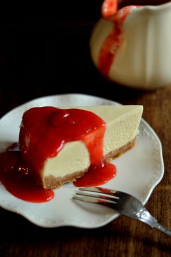 Delicious raspberry coulis decorates and garnishes a scrumptious vanilla cheesecake, served on a vintage porcelain plate on an antique oak table.