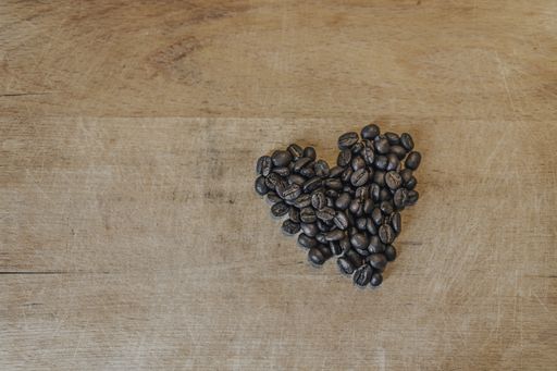 Shape of heart made of roasted coffee beans on a wooden surface. Close up shot of coffee beans shaped to a heart.