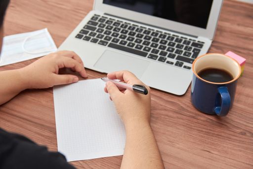 A high angle shot of female hands with pen and paper and a laptop on office desk