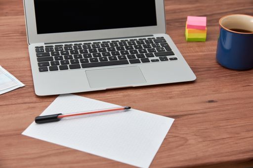 A high angle shot of a working desk with laptop and paper and pen with a cup of coffee