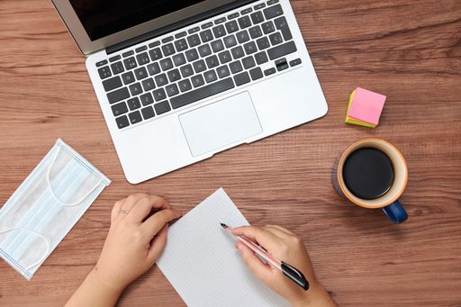 An overhead shot of female hands with pen and paper and a laptop on office desk
