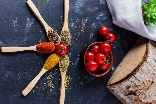 The wooden spoons with spices, paprika, basilic, pepper, thyme with cherry tomatoes