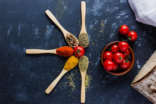 The wooden spoons with spices, paprika, basilic, pepper, thyme with cherry tomatoes