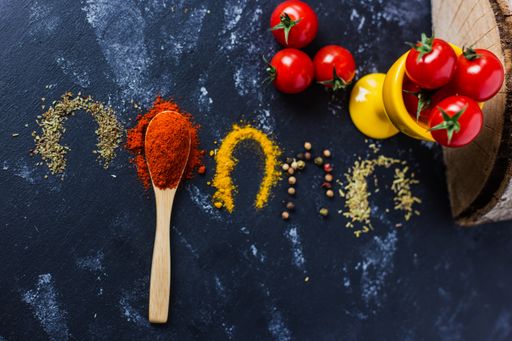 A spoon and spices with cherry tomatoes on a dark table
