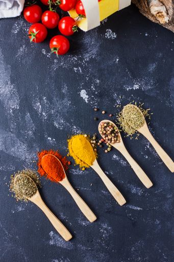 The wooden spoons with spices, paprika, basilic, pepper, thyme with cherry tomatoes