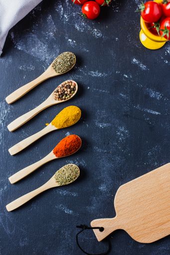 The wooden spoons with spices, paprika, basilic, pepper, thyme with cherry tomatoes