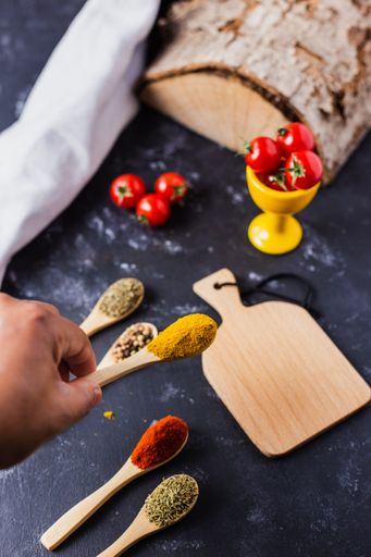 A hand holding a wooden spoon with spices and cherry tomatoes on the table