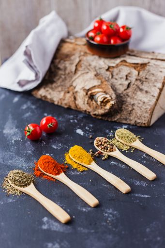 The wooden spoons with spices, paprika, basilic, pepper, thyme with cherry tomatoes