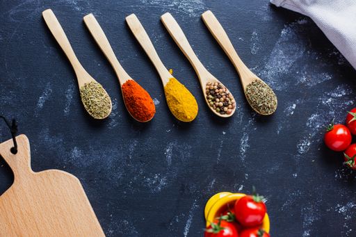 The wooden spoons with spices, paprika, basilic, pepper, thyme with cherry tomatoes