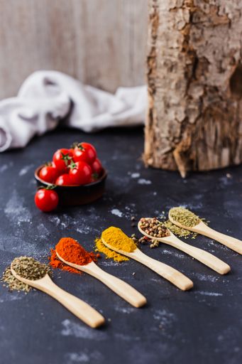The wooden spoons with spices, paprika, basilic, pepper, thyme with cherry tomatoes