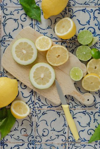 A close-up image of a cutting board with various citrus fruits and green foliage