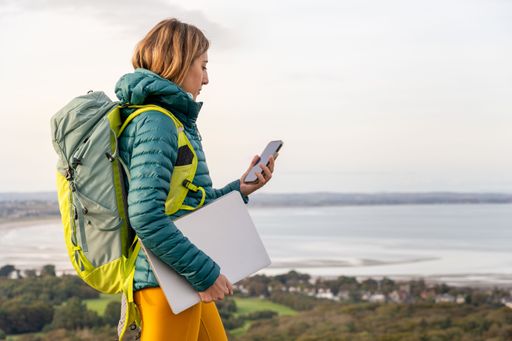 A young female adult is pictured standing on a hilltop, wearing a pair of bright yellow trousers and holding a backpack