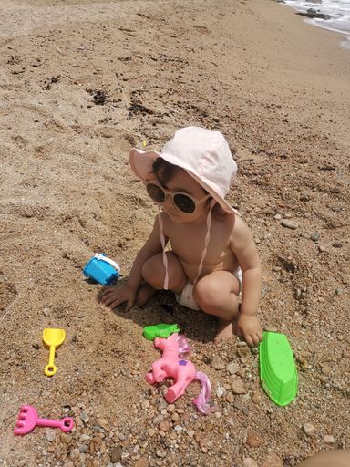A closeup of a  child playing with toys on the sun-soaked beach, with the ocean in the background