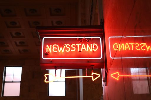 A glowing yellow sign featuring the words 'Newsstande', 'Chatsweld' and 'Directions'