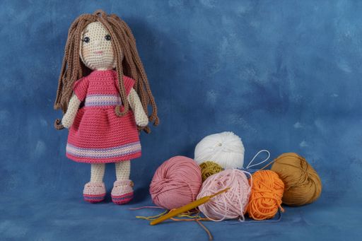 A cute amigurumi doll handmade on a blue background with balls of yarn