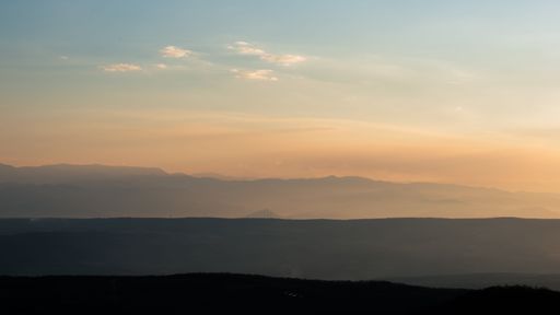 A stunning landscape featuring a picturesque sunset behind a series of snow-capped mountains.