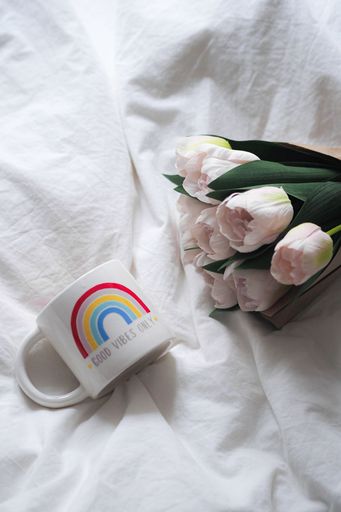 A cozy bedroom scene with a white pillow, a ceramic mug, and a vibrant pink tulip on a bed