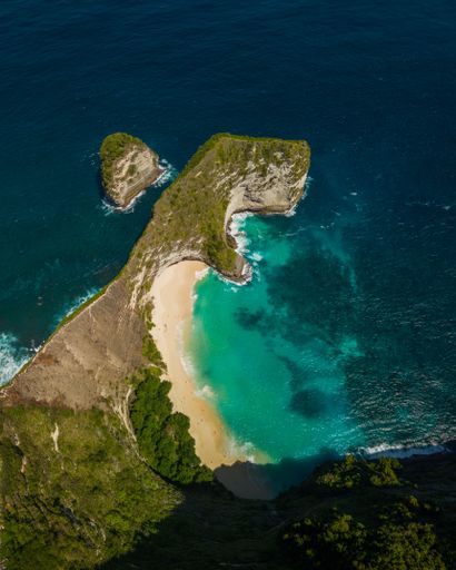 A dramatic landscape with two majestic rock formations overlooking the turquoise ocean from the edge of the sandy beach