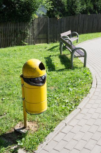 A vertical shot of a yellow trash bin in a park