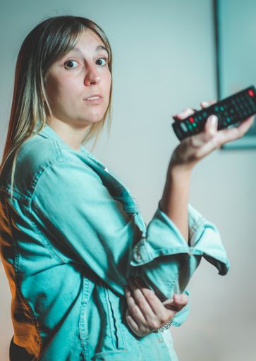 A young pretty blonde Argentinian woman with a surprised face holding a remote controller