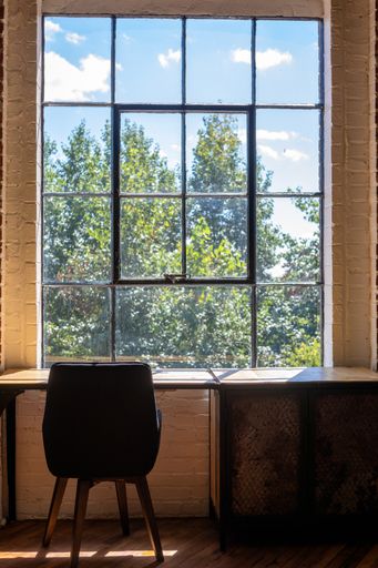 A vertical shot of a chair and a desk near a large window with an amazing view of greenery outside