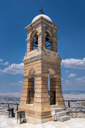 A picturesque church bell tower is situated atop a sturdy stone slab, surrounded by a clear blue sky