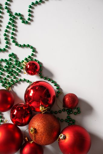 An image of a festive red ball Christmas tree set up on a table, decorated with green ornaments and beads
