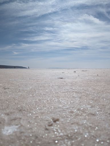 A man is traversing a sandy landscape with a surfboard under his arm