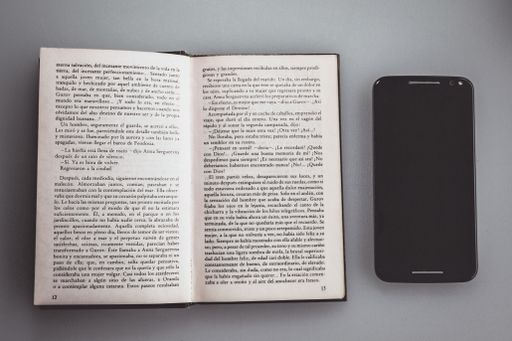 An overhead shot of an open book next to a phone