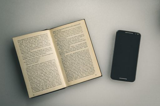 An overhead shot of an open book next to a phone