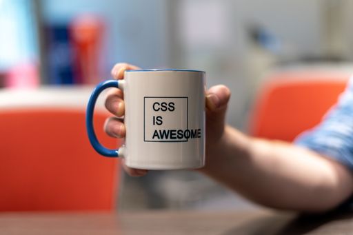 A selective focus shot of a person holding a mug with a printed text of "CSS IS AWESOME" with a blurred background
