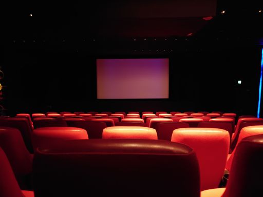 An auditorium with red chairs and a large white projection screen in a dimly lit room