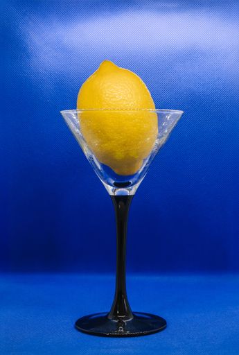 A closeup of a yellow lemon in a martini glass set against a vivid blue background.