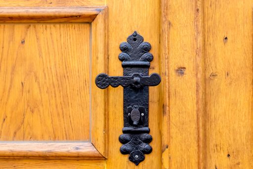 A closeup shot of a black vintage metal door handle on a brown wooden door