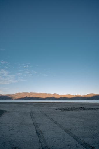 A vertical shot of a field roadway that goes to a lake and a mountain on the background
