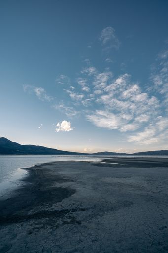 A beautiful shot of a lake and a beach surrounded by hills and a cloudy sky