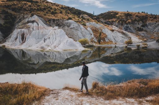 A beautiful shot of a man walking near Blue Lake surrounded by hills under a blue sky in New Zealand