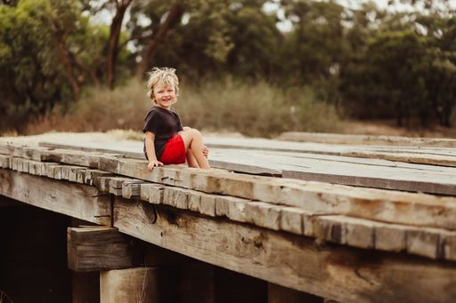 A shallow focus shot of a little boy sitting on a wooden pier