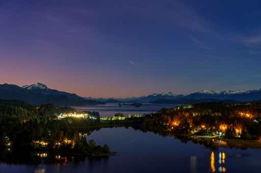A tranquil lake scene illuminated by the soft light of dusk and a waxing crescent moon