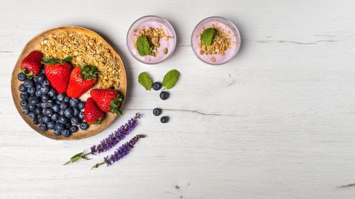 Top view of two bowls of berries yogurt and a wood plate  with strawberries and blueberries for healthy breakfast on a rustic white table background.