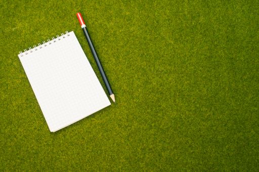 A top view shot of a spiral notebook and a pen on a green grass surface
