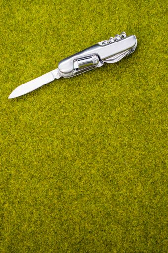 A top view shot of an open steel pocket knife on a green grass surface