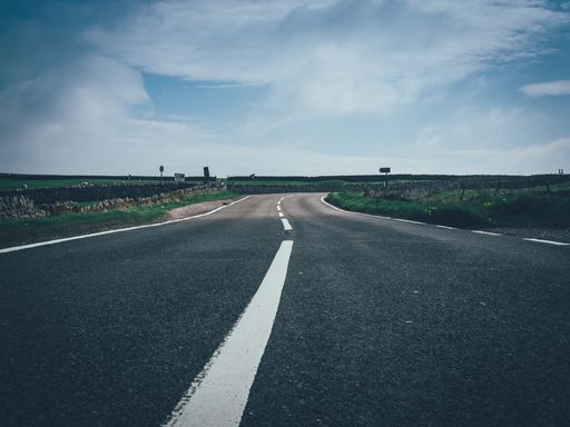 A beautiful shot of a concrete road with a white line in the middle of a large field  with beautiful sky