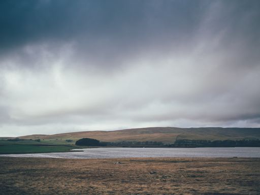 A beautiful shot a large field with hills and a lake during a rainy day in the countryside