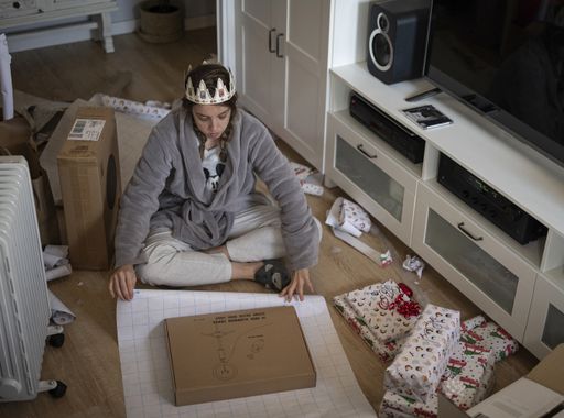 A young Spanish woman wrapping Christmas gifts at home while sitting on the floor