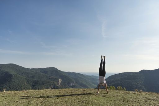 A young Spanish woman doing a handstand on top of the mountain