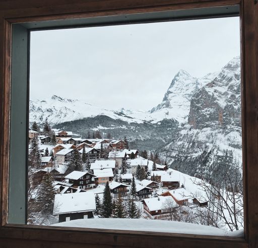 A beautiful view from a wooden window frame - small buildings in a village with snow-capped roofs